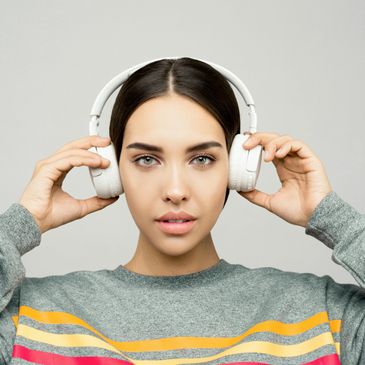 Young woman wearing white headphones and a colorful striped sweater.