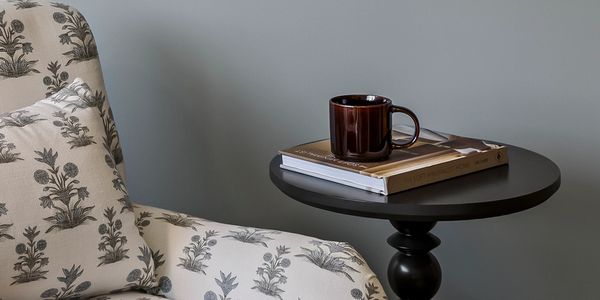 Cozy chair with floral cushion next to a round table with a cup.