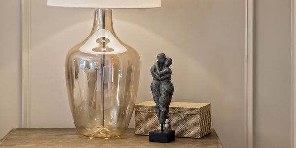 Glass lamp and embracing sculpture on wooden table.