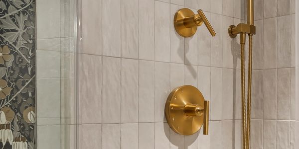 Modern shower with gold fixtures and beige tiles.