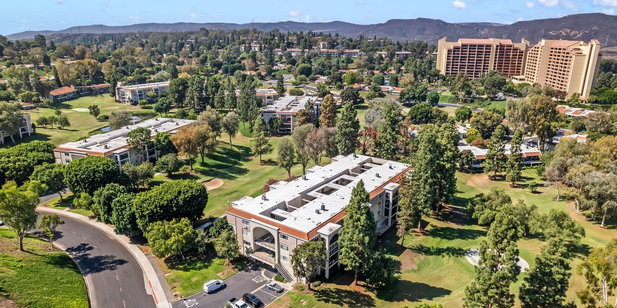 A scenic view of a green golf course with surrounding residential buildings and hills.