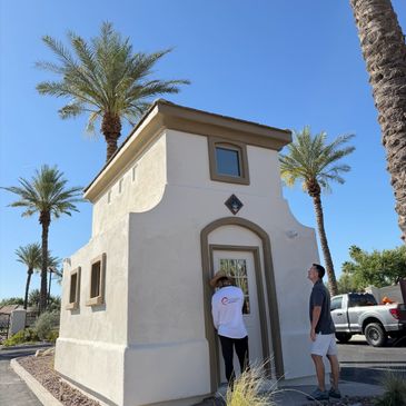Two people standing near a small desert-style building with palm trees around.