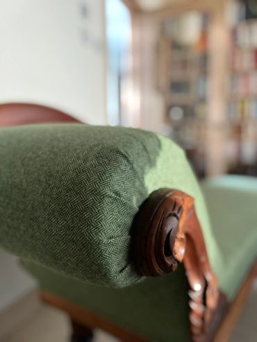 Close-up of a green upholstered armrest with wooden details.