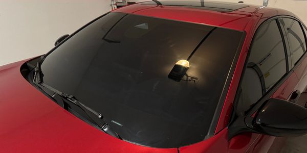 Red car with heavily tinted windshield and windows in a garage.