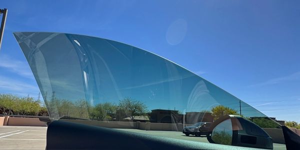 Car window partially rolled down showing clear blue sky and trees outside.