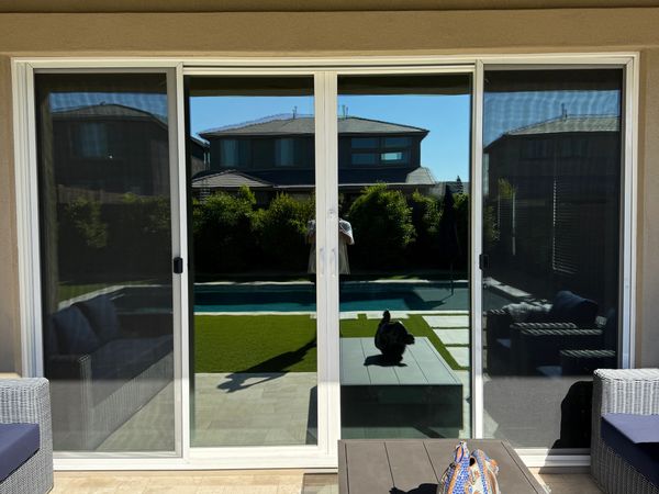 Glass sliding door reflecting a backyard with a pool and patio furniture.