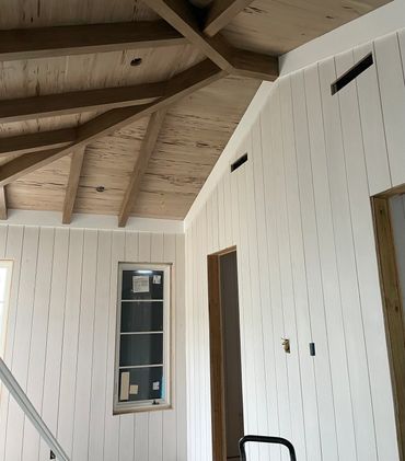 Interior of a room under construction with wooden ceiling beams and white paneled walls.