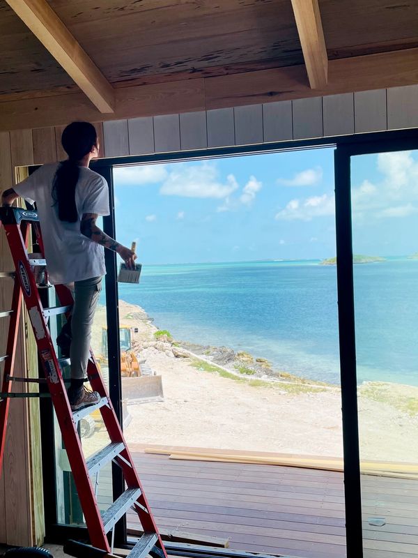 Person painting near a large window overlooking a serene ocean view.