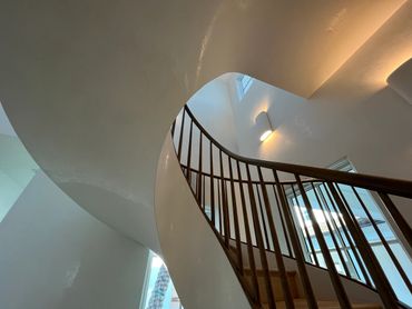 Curved wooden staircase with modern white walls and soft lighting.