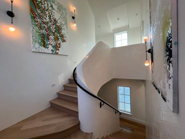 Curved staircase with wooden steps and modern wall art in a bright, minimalistic space.