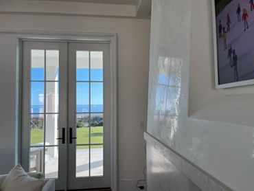French doors open to a sunny patio with a lawn and ocean view.