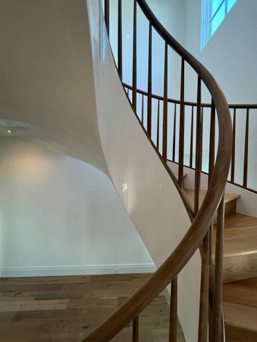 Elegant wooden spiral staircase with white walls and natural light.