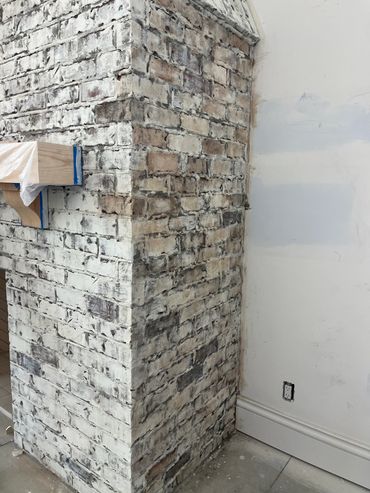 Partially whitewashed brick chimney with wood details and unfinished wall.