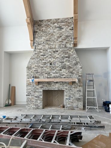 Unfinished brick fireplace with ladders and construction tools in a room under renovation.