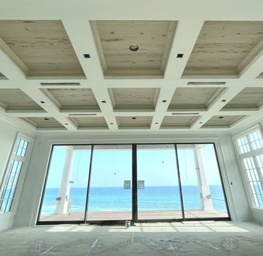 Room with wooden coffered ceiling and ocean view through large glass doors.
