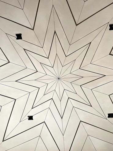 Intricate geometric star pattern on a ceiling with small square openings.