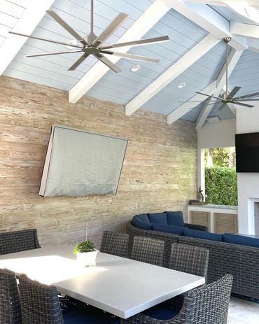 Cozy outdoor patio with wicker furniture and ceiling fans under a blue vaulted ceiling.