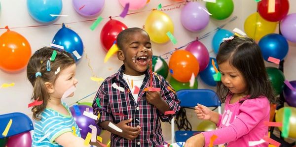 Three children enjoying a colorful birthday party with balloons and confetti.