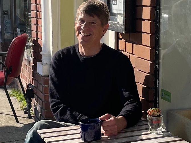 Ken White, smiling, seated at an outdoor coffeeshop table.