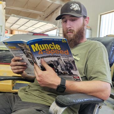 Tomas holds a Muncie 4‑speed transmission workbook, preparing for manual rebuild tasks.