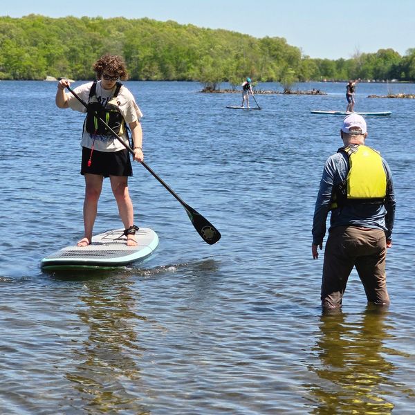 People paddleboarding on a lake with safety vests on a sunny day.