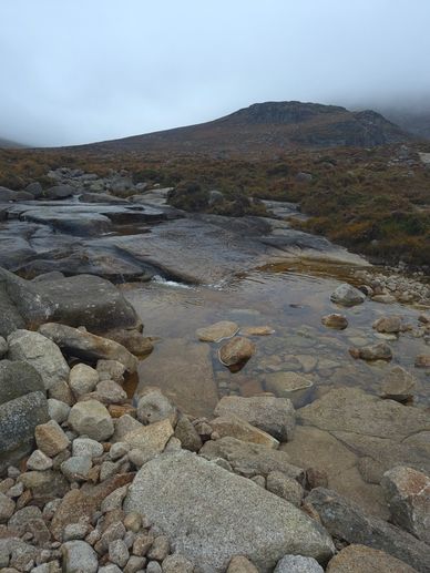 Rocky landscape with water and misty hill.