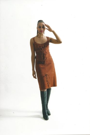 Woman in a brown dress and black boots posing against a white background.