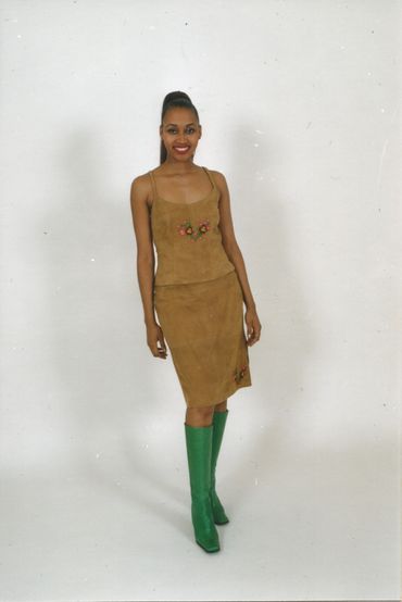 Woman in a brown dress and green boots posing against a white background.