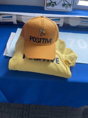 Yellow cap and shirt with 'POSITIVE' and bee design.