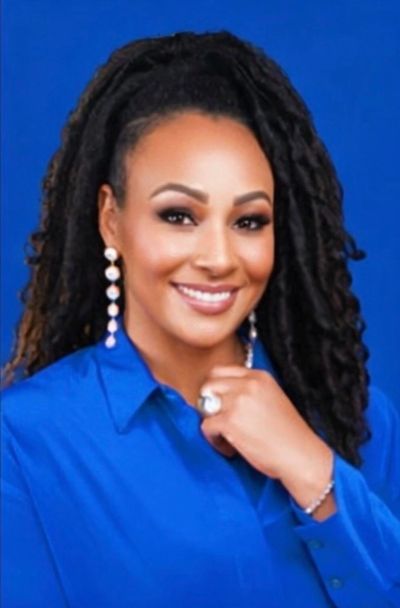 Smiling woman with long curly hair in blue shirt and pearl earrings.
