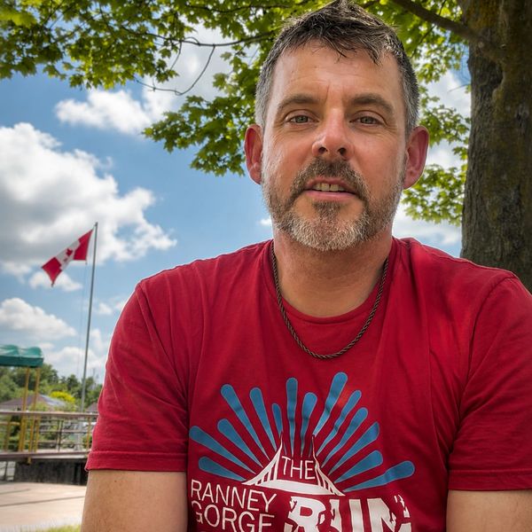 Man in a red shirt outdoors with a Canadian flag in the background.