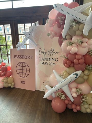 Travel-themed baby shower setup with balloons, planes, and a passport prop.