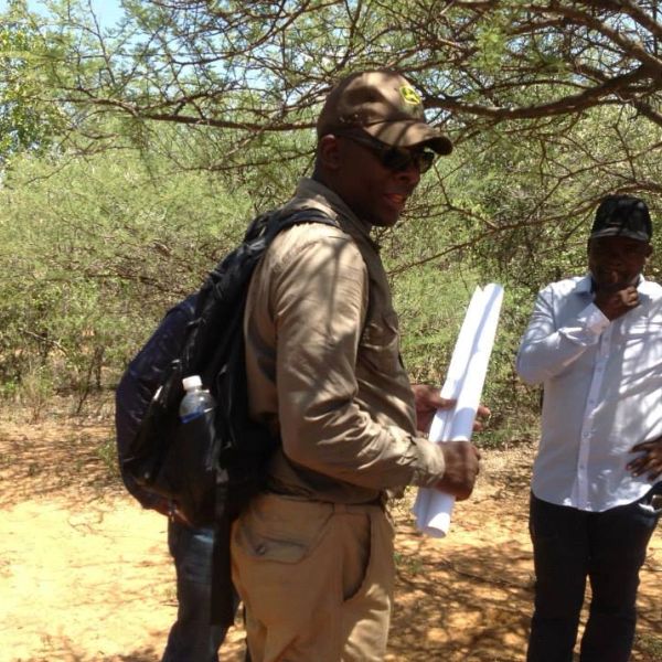 Man holding rolled papers in a wooded area.