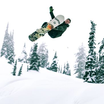 Snowboarder performing a high jump in a snowy forest.