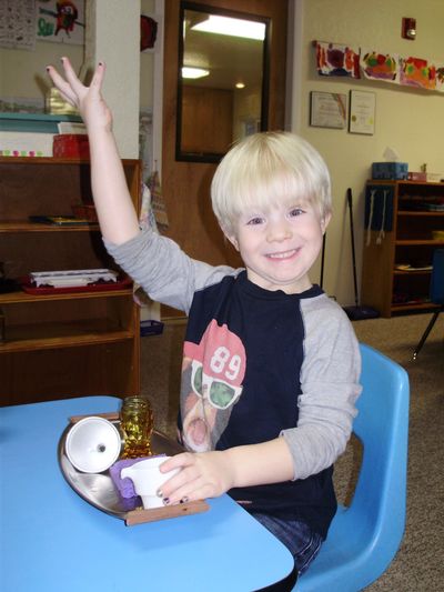 Young boy smiling and raising his hand in a classroom.