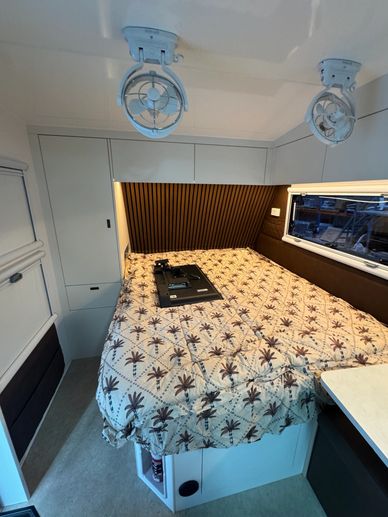Cozy camper van bed setup with palm tree bedding and overhead fans.