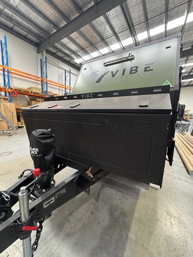 Black Vibe camper trailer in an industrial warehouse setting.