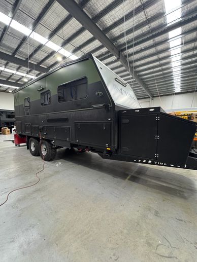 Black off-road camper trailer inside a warehouse with dual axles.