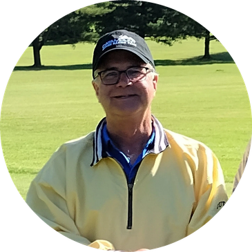 Smiling man in yellow jacket and black cap on golf course.