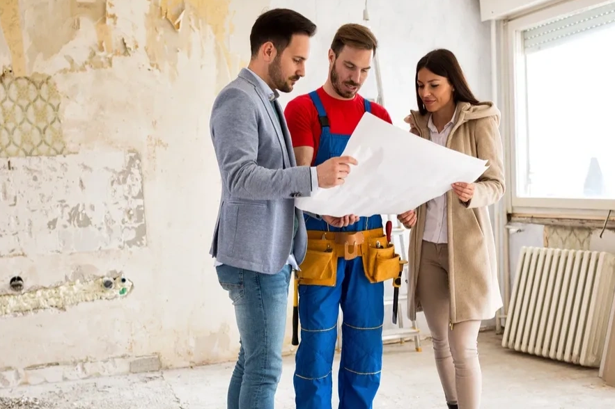 A couple and a contractor review renovation plans inside a damaged room.