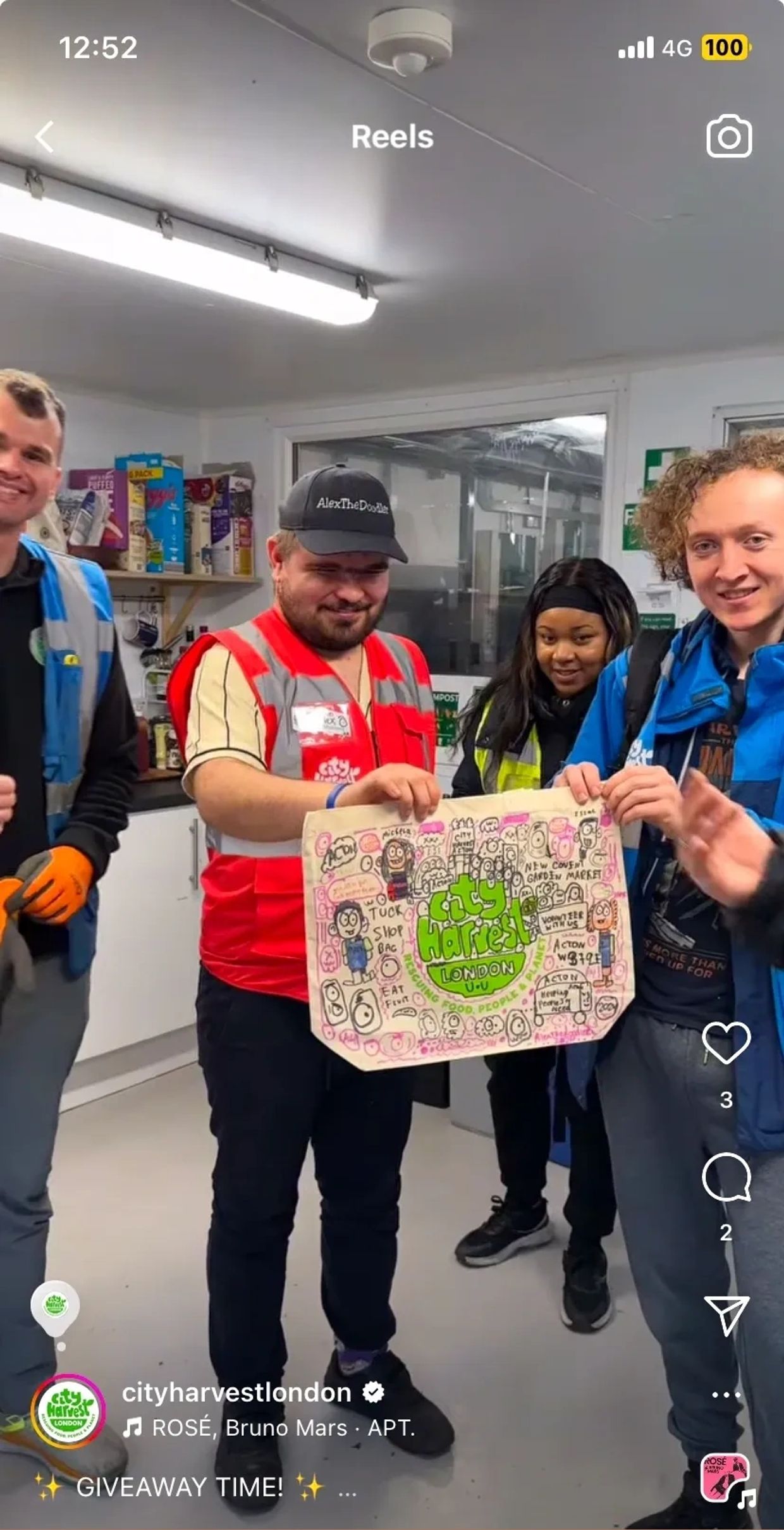 Volunteers holding a decorated City Harvest London bag inside a food storage room.