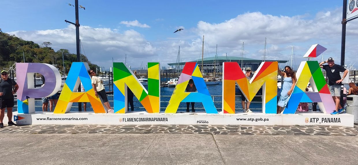 Colorful PANAMA sign with people posing by the waterfront under a bright sky.