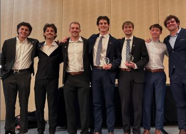 Seven men in suits posing with awards, smiling and standing close together.