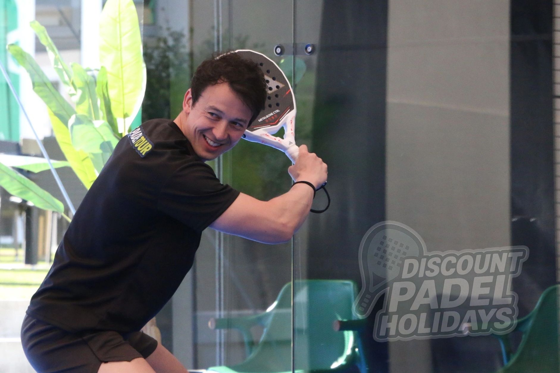Smiling man holding a padel racket preparing to hit the ball indoors.