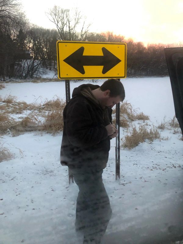 Man standing in front of a two-way arrow sign in snowy landscape.