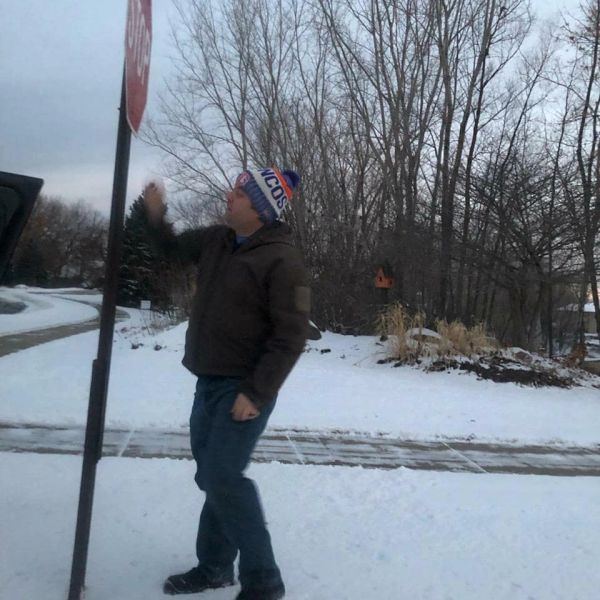 Man in winter clothes standing near a stop sign in snowy setting.