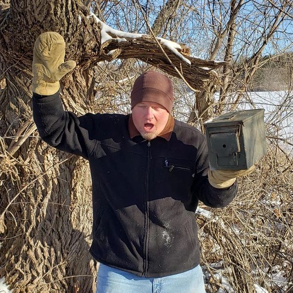 Man in winter gloves holding a rusted metal box with a surprised expression.