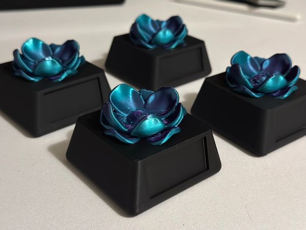 Four black keycaps with metallic blue flower designs on top.