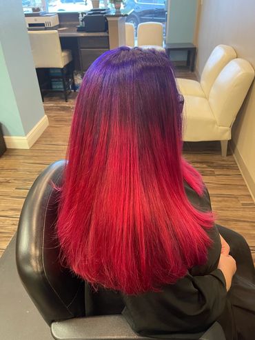 Woman with purple and red ombre hair sitting in a salon chair.