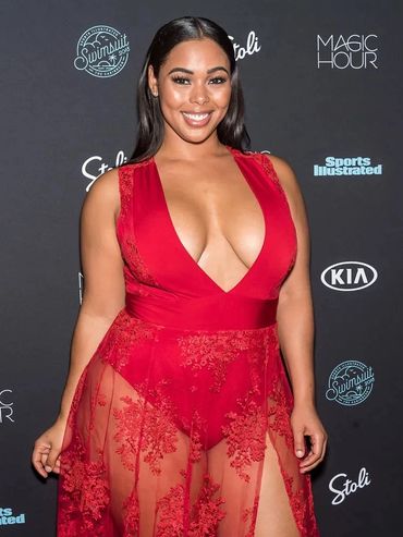 A woman in a red lace dress poses at a Sports Illustrated event.